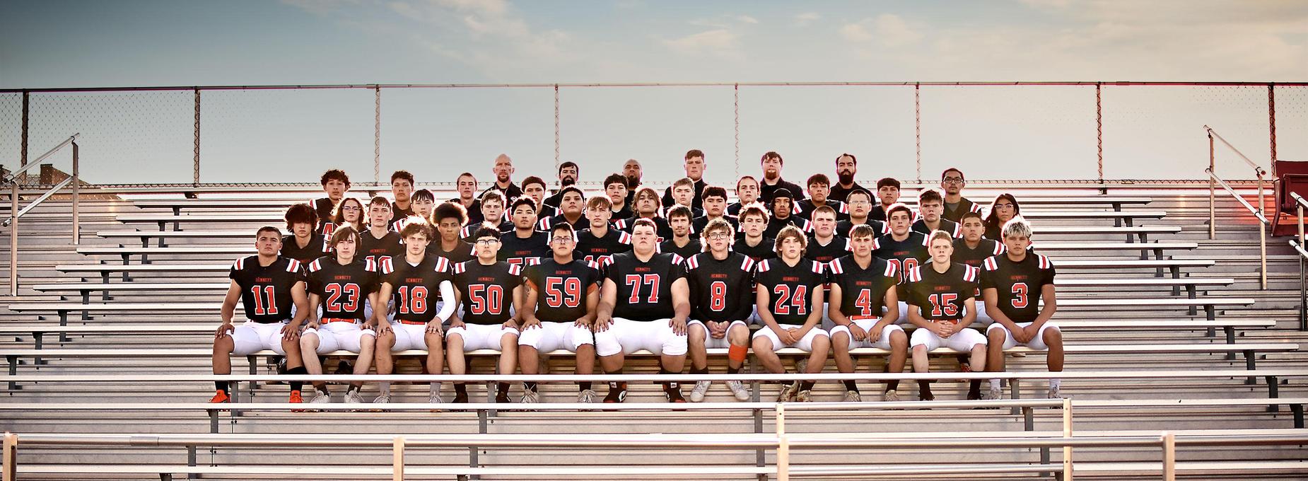 Team photo of a high school football squad on bleachers, wearing black and orange uniforms.