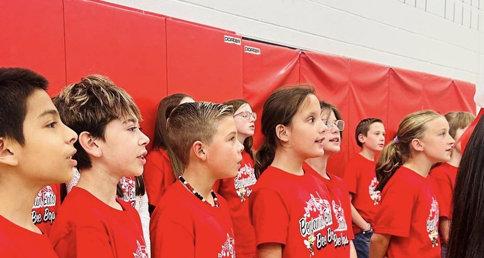 Children singing in red shirts during a performance.