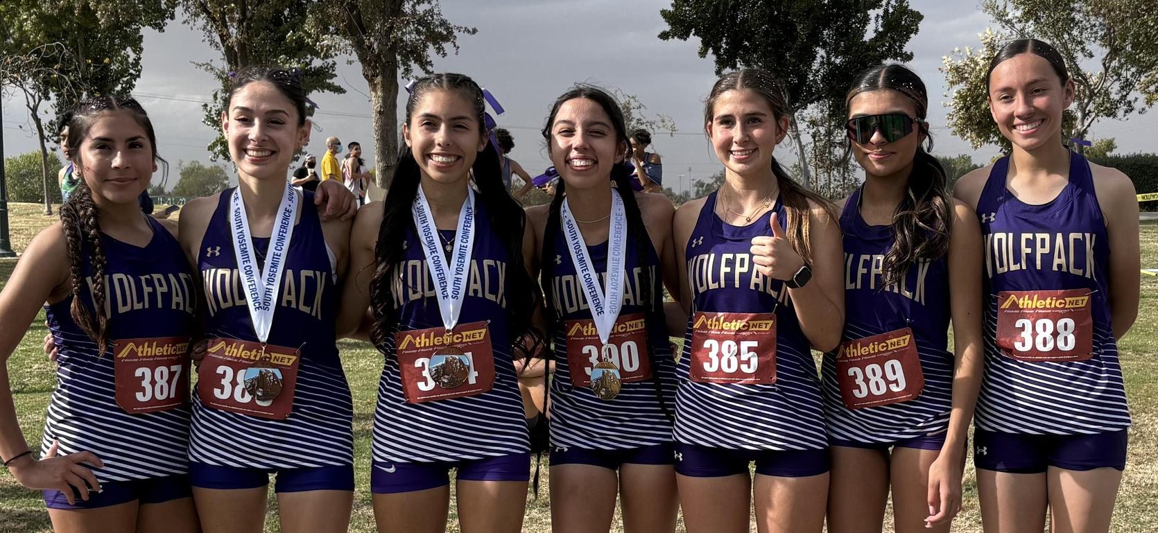 Six female athletes dressed in racing uniforms with medals at an outdoor event.