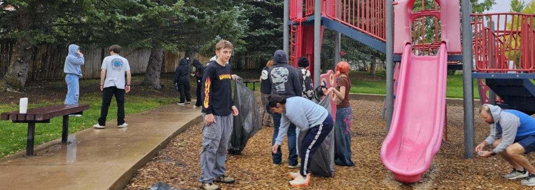 Teens enjoy a community clean-up event near playground equipment.