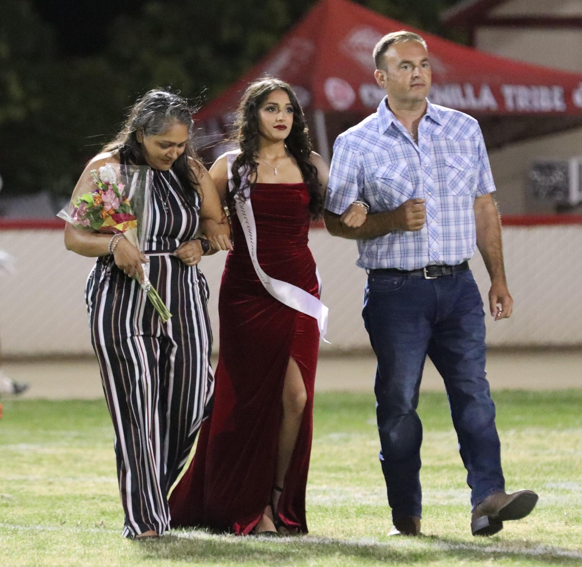 homecoming king and queen candidates walking across the field with their escorts
