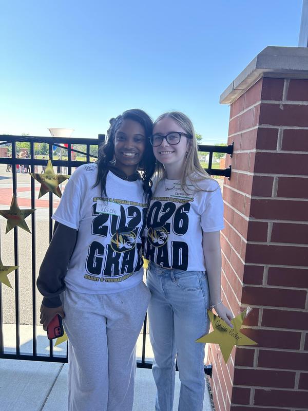 wo smiling high school students pose together outdoors wearing matching white 