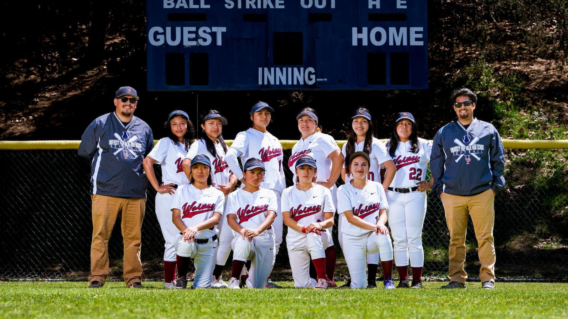 A girls' softball team poses together in front of a score board.