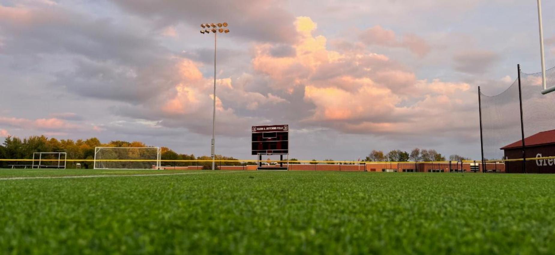 Soccer field with artificial turf and a cloudy sunset sky in the background.