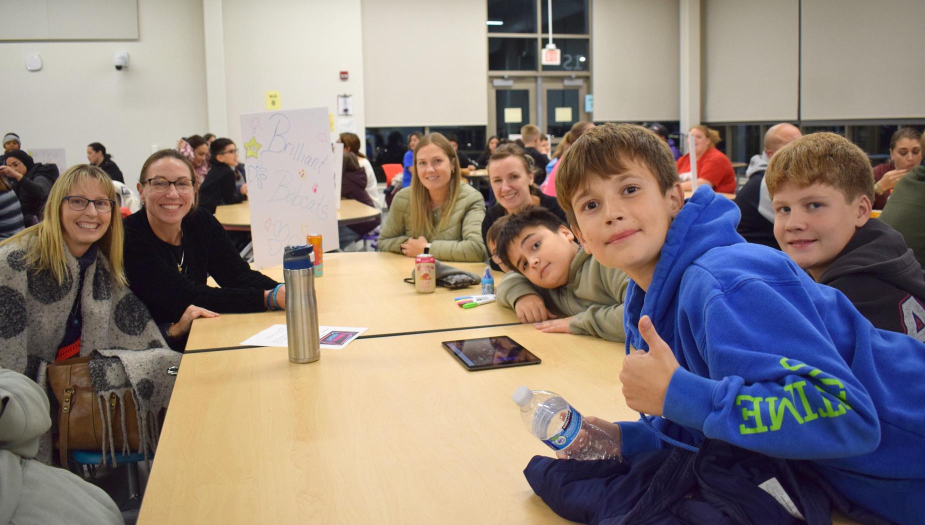 A cheerful group of adults and children at a table, posing with smiles and drinks at a gathering.