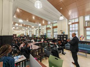 Audience listening attentively in a large room with seating and artwork.