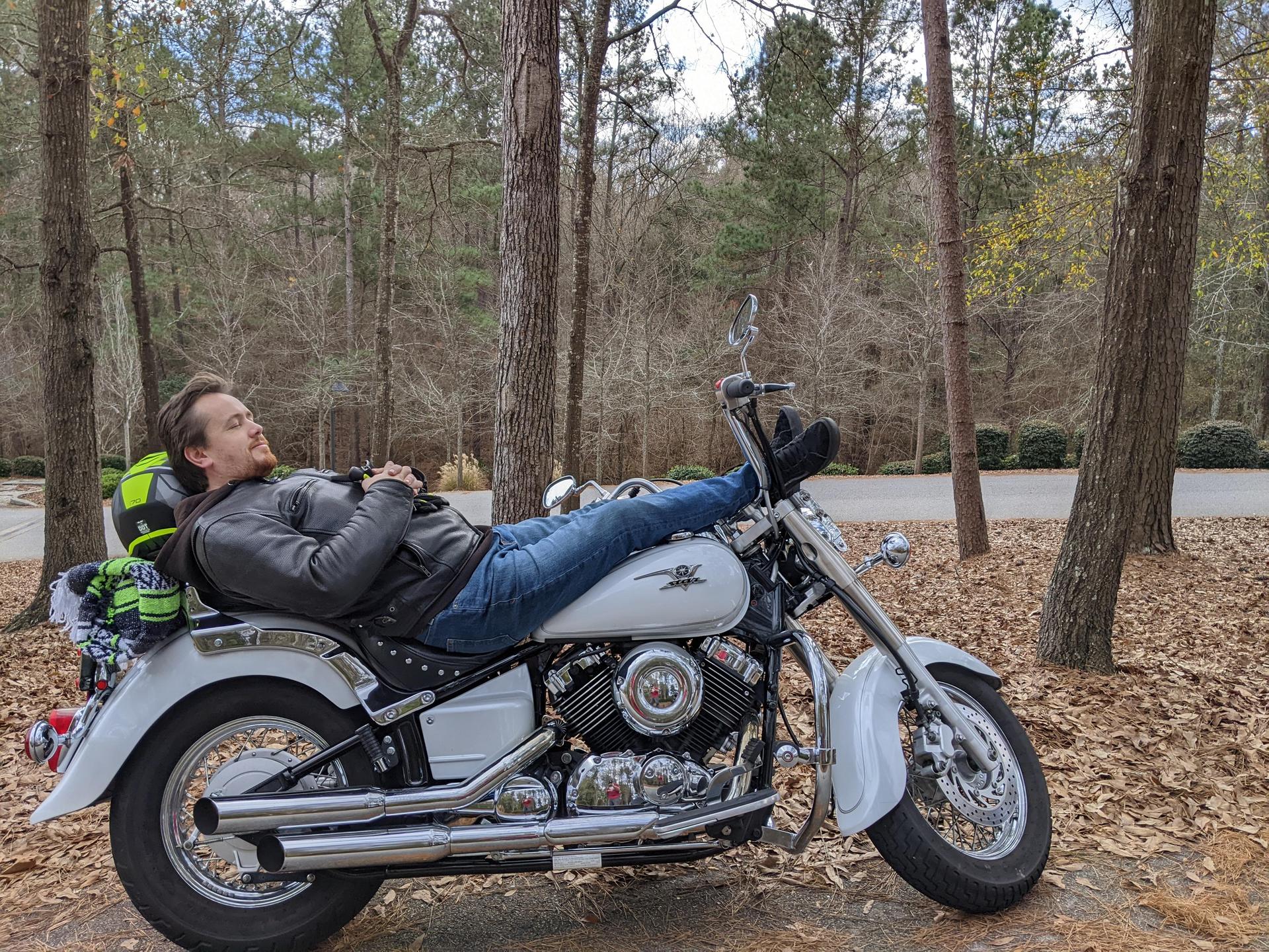 Man laying asleep across the top of a motorcycle