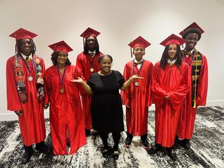 Smiling child in a white graduation gown holding medals, standing proudly at a graduation ceremony.