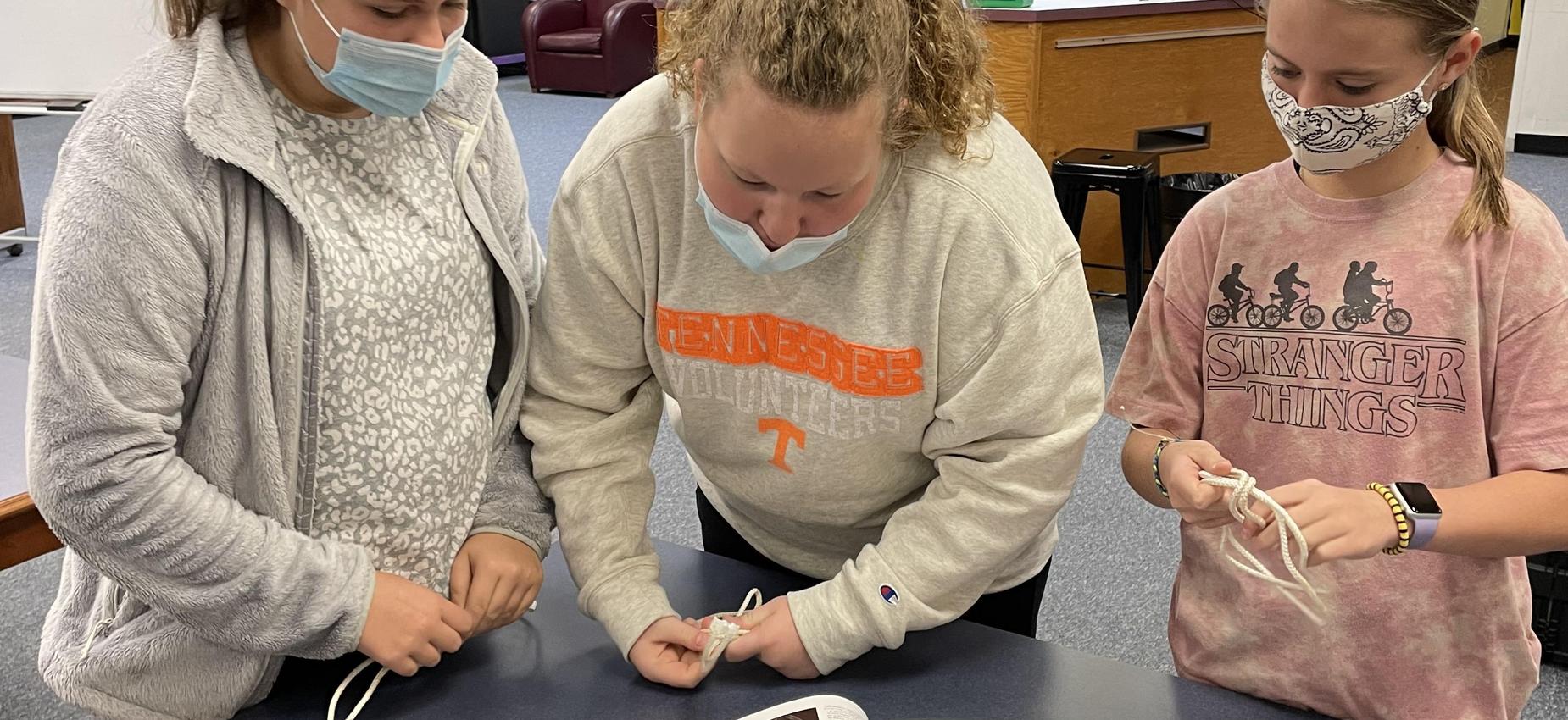 Three students tie knots in a library.