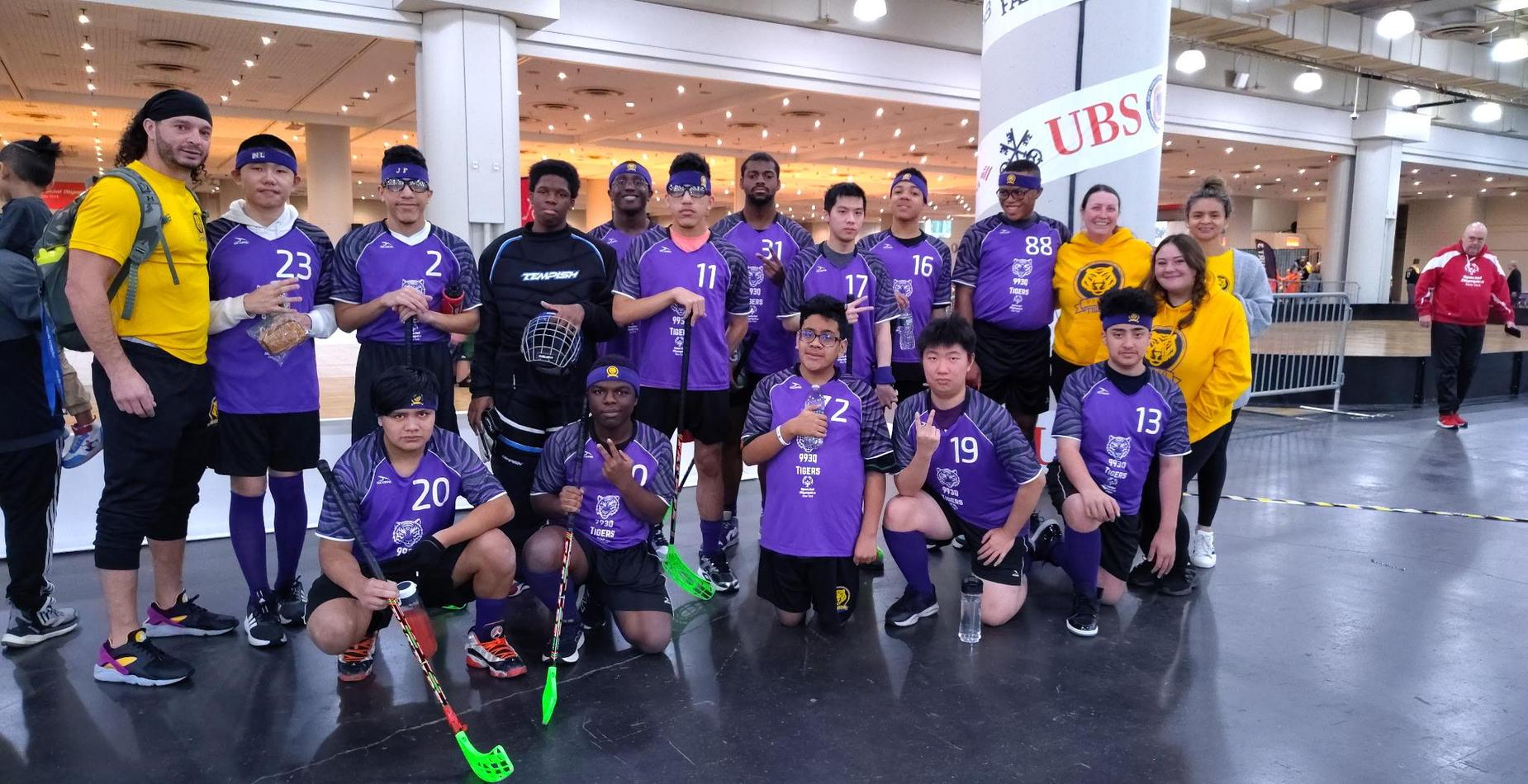 A team of athletes in purple uniforms posing together at an event venue.
