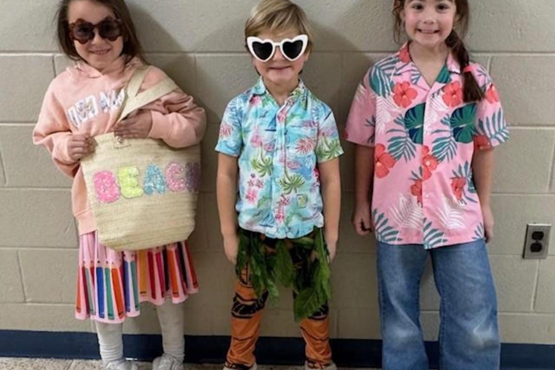 Three kids in tropical outfits with sunglasses and bags, posing cheerfully.