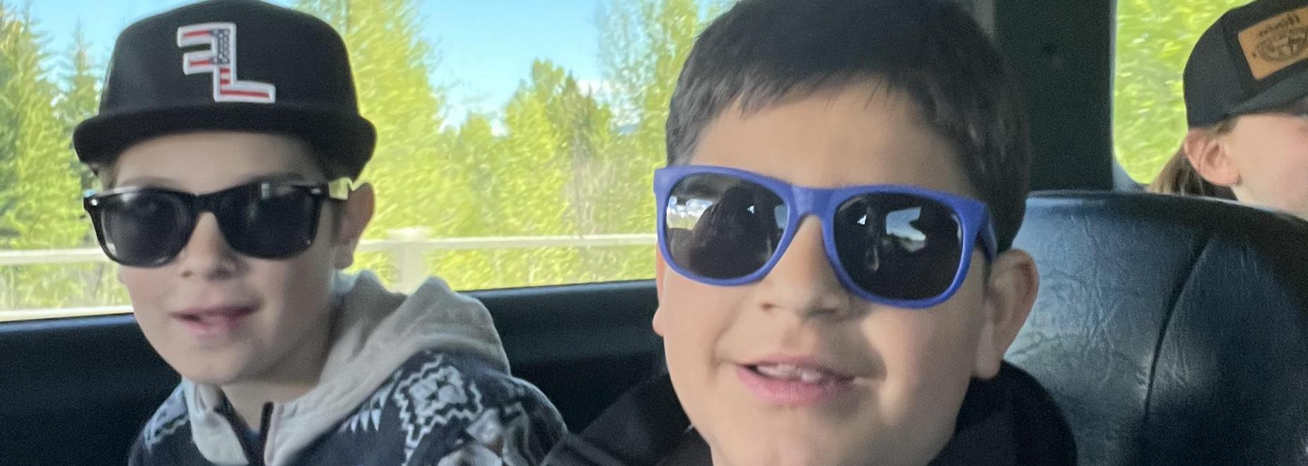 Two boys wearing sunglasses smiling in a vehicle with a scenic view.