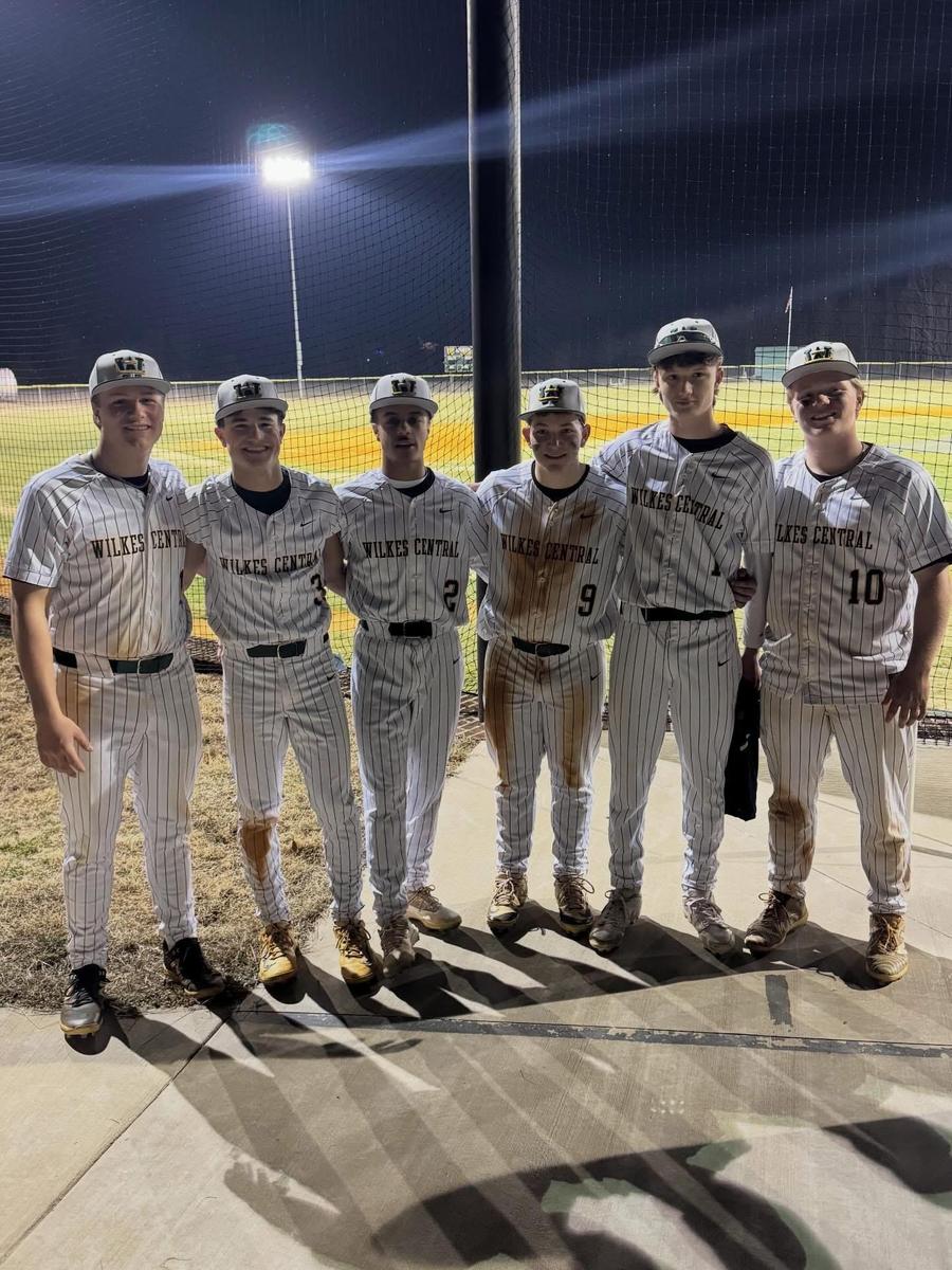 Six young baseball players posing together in their uniforms at the field.