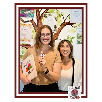 A woman with glasses and a book, and another women pose for a photo.