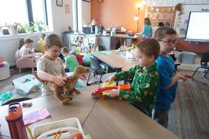 Two students play with a dinosaur and a car carrier.