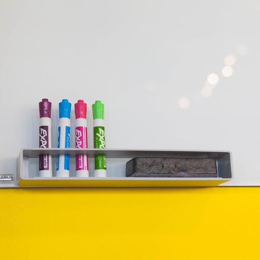 Colorful dry-erase markers and an eraser on a whiteboard shelf.