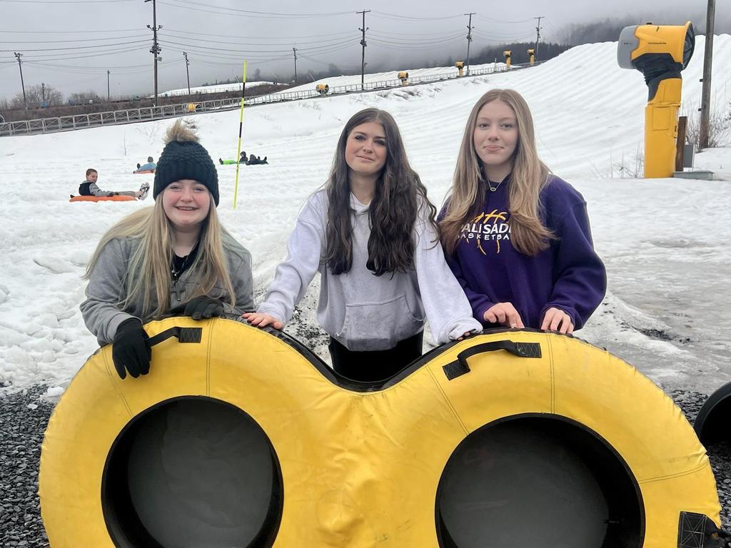 Three students holding up an inner tube with a snowy slope in the background.