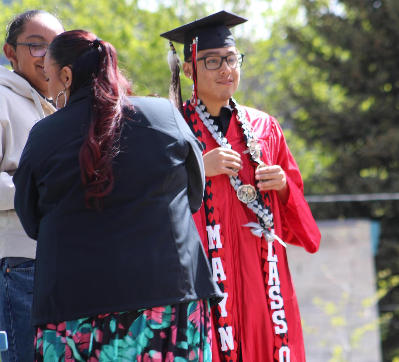 Graduate in red gown with ornaments, posing with a person in a black jacket.