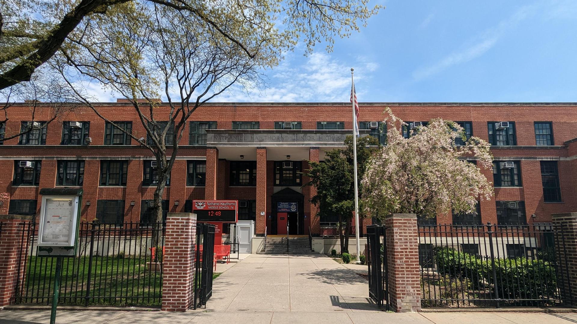 Red brick school building with trees, flag, and landscaped front entrance.