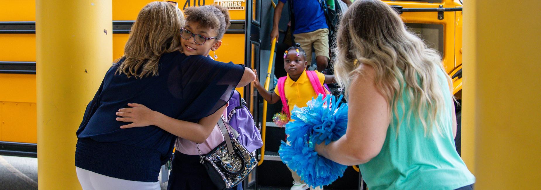 A student hugs a teacher as she gets off the bus for school