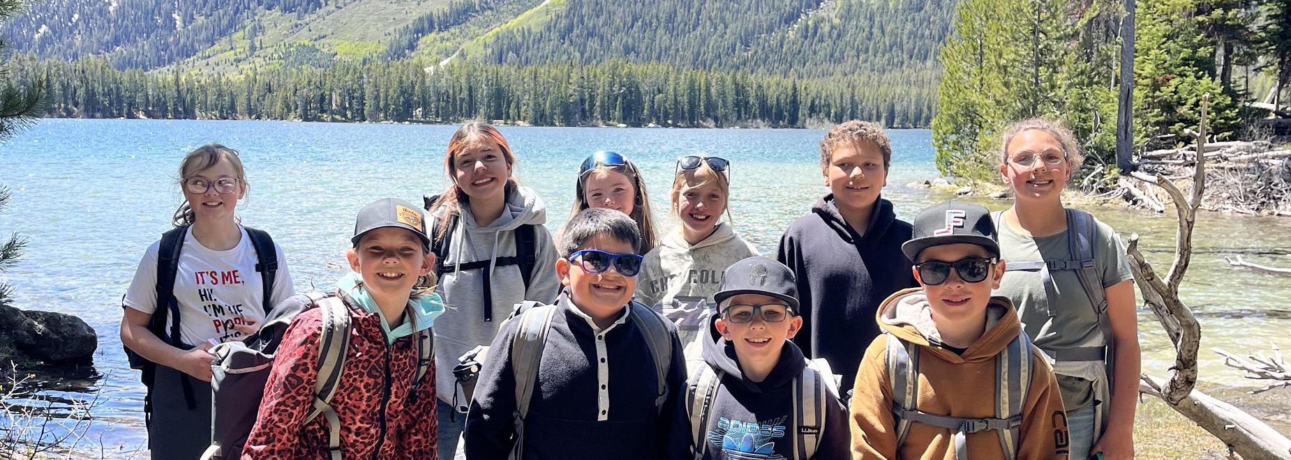 Group of children smiling near a lake with mountains in the background.