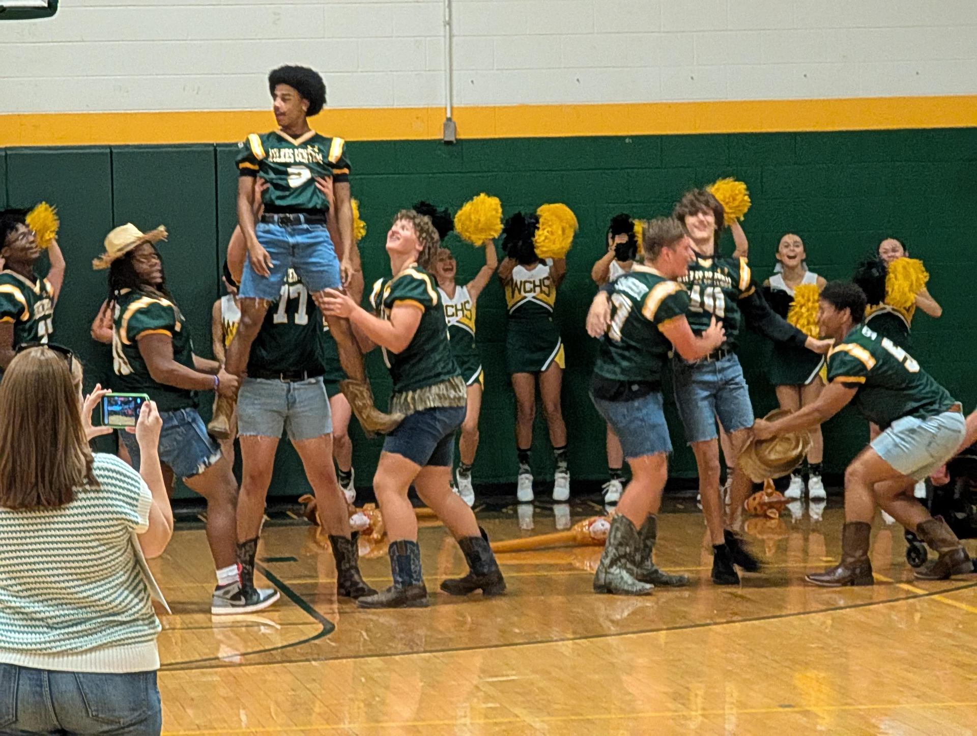 Cheerleaders and students in costumes celebrate at a school event with cheering and lifting.