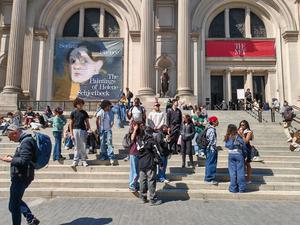 A crowd of visitors at the steps of a museum with banners and artworks.