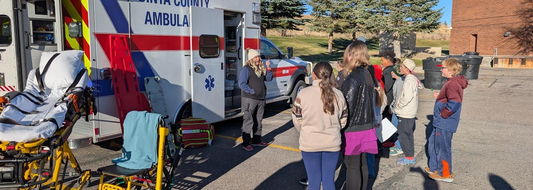 Group of kids watching a presentation by a medic outside an ambulance.