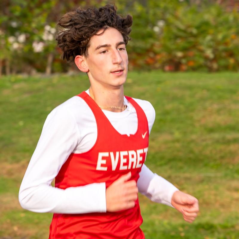 A young runner in a red athletic uniform jogging on a grassy area.