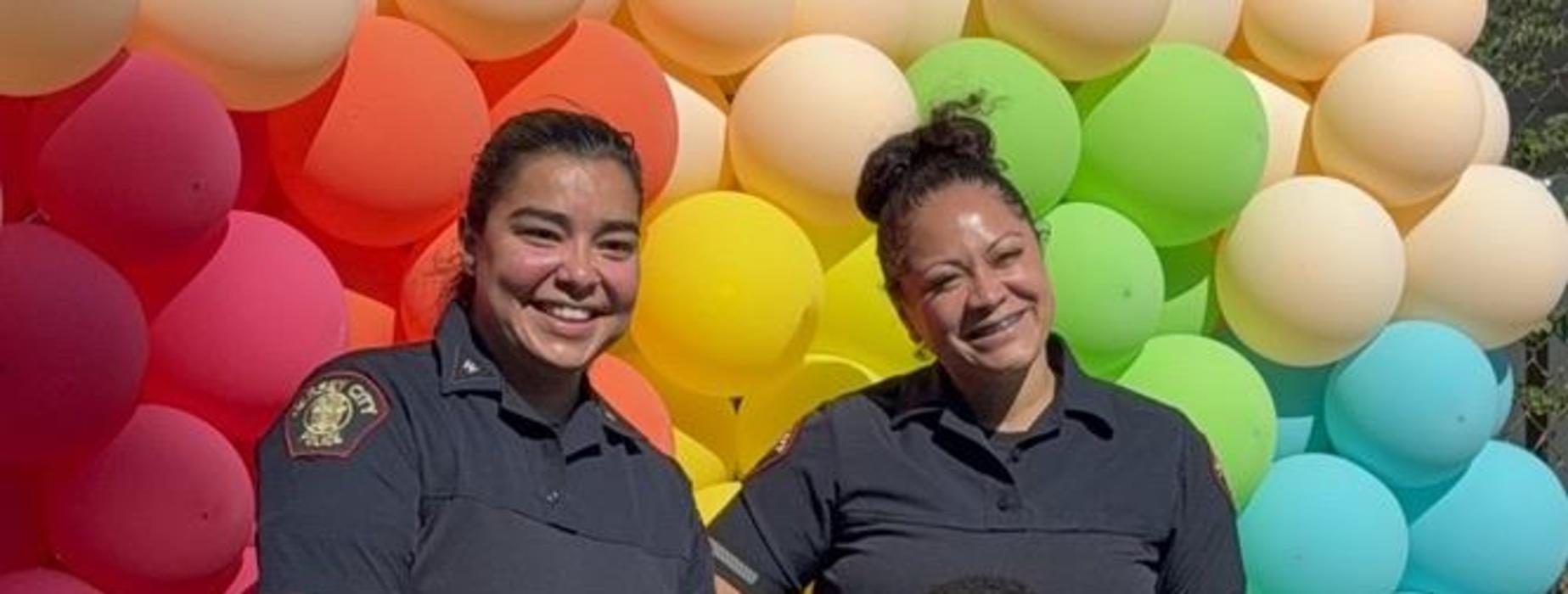 Two police officers and a young boy pose together in front of colorful balloons.