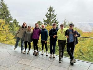 Group of seven young people posing outside with a colorful landscape in the background.