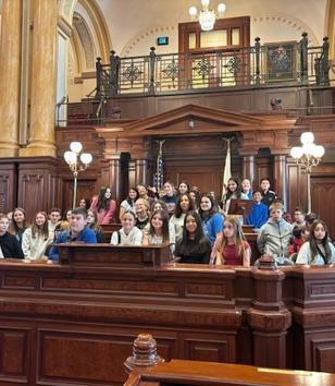 Group of students posing in a historic legislative chamber.