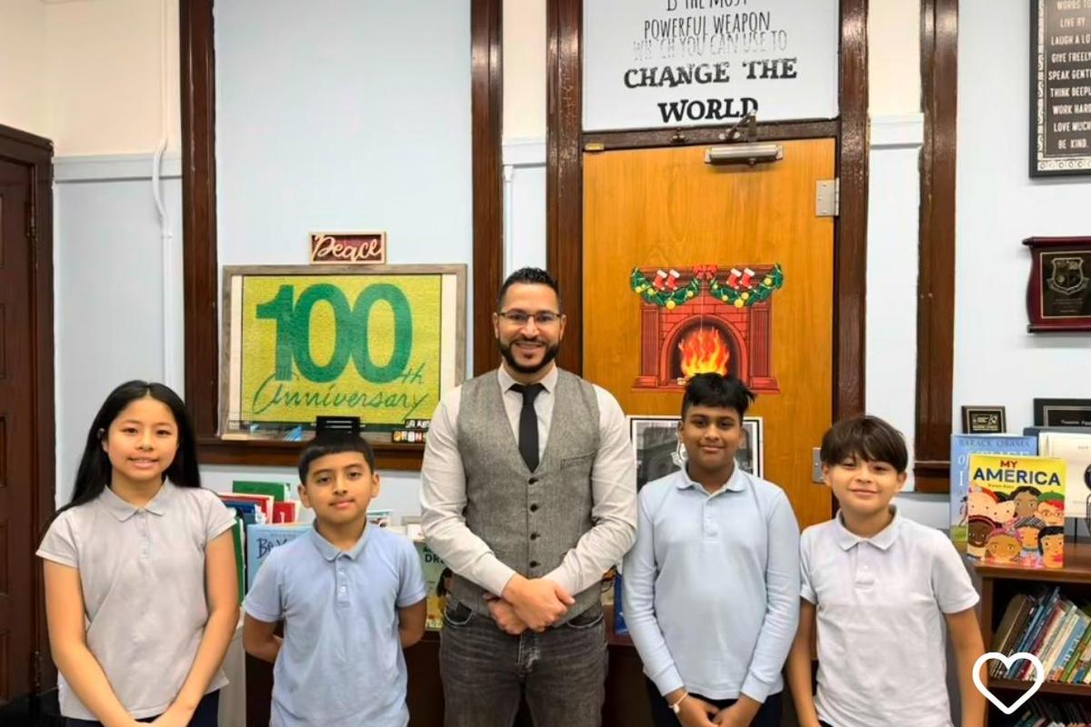 Four students and a teacher standing together in front of a school door with a sign celebrating an anniversary.