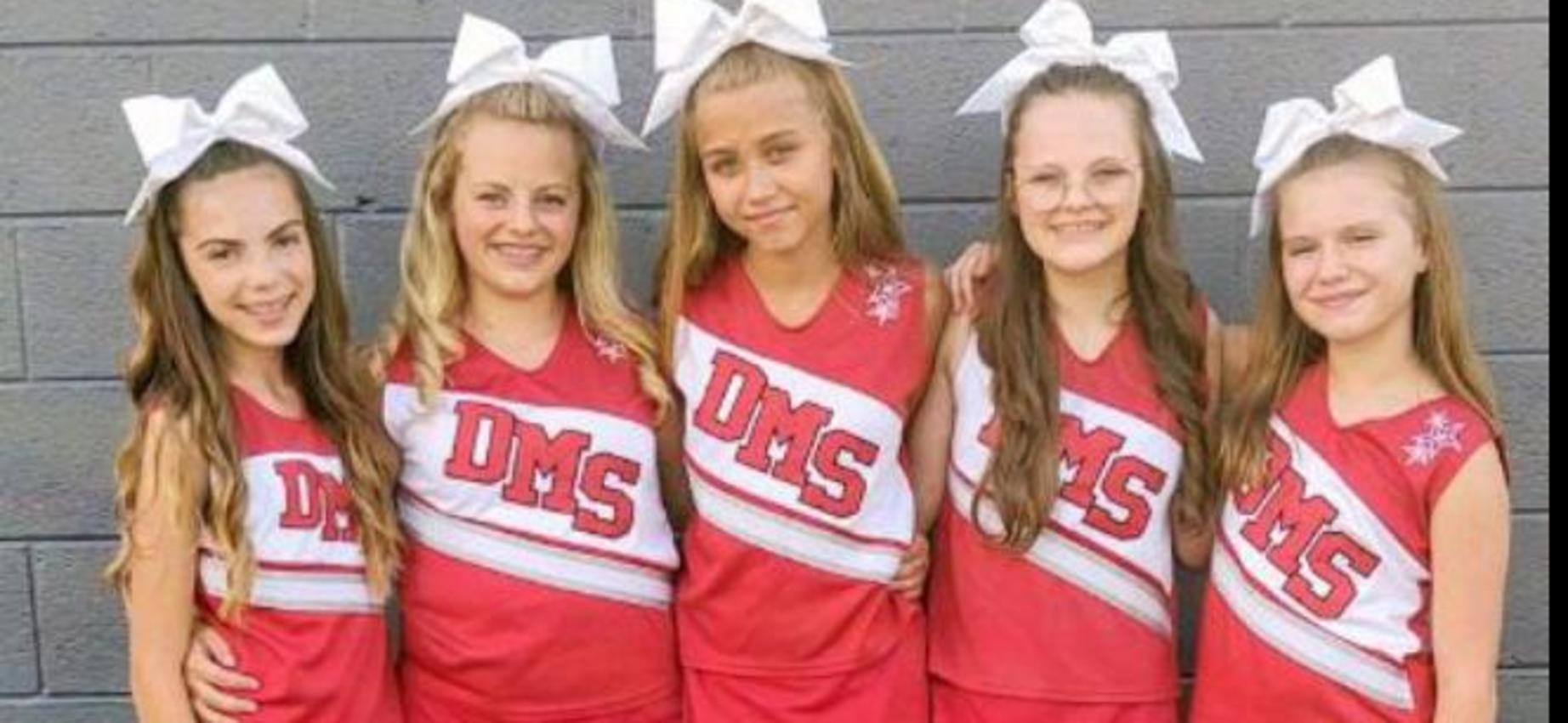 Cheerleaders stand in front of a wall.