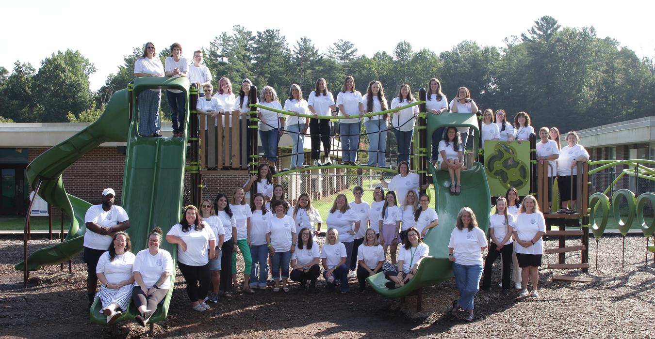 Group of people in white shirts posing on playground equipment.