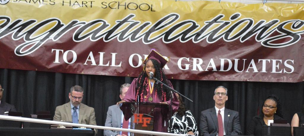 girl addresses audience from podium while school board members look on