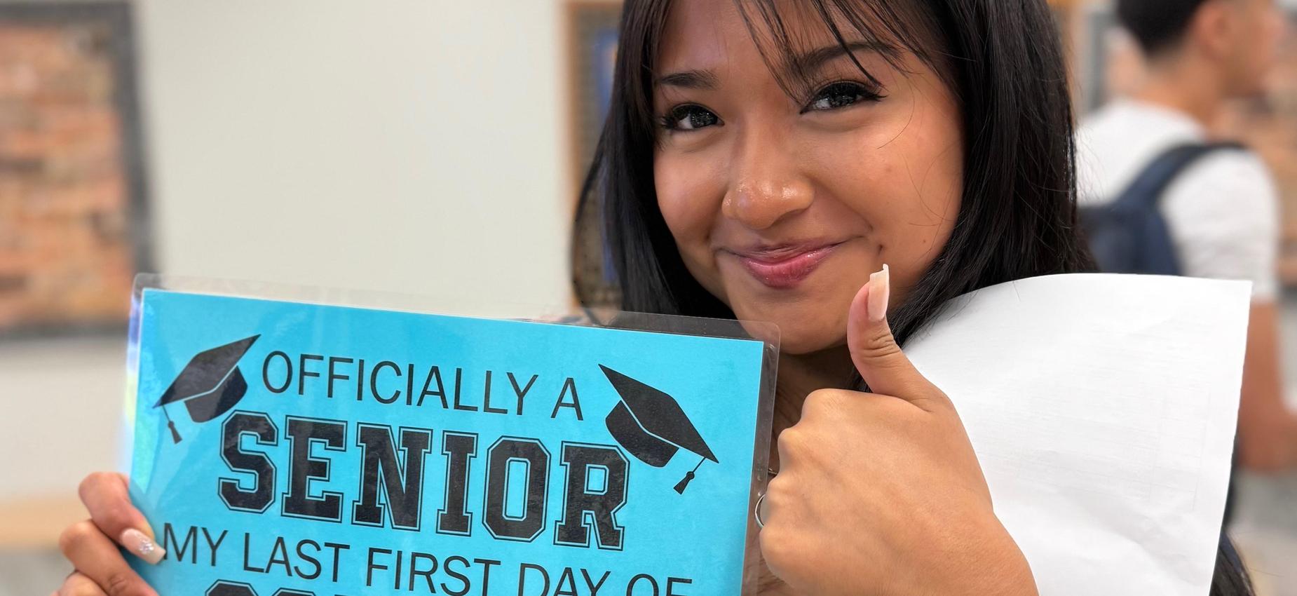 A students holding an "Officially a senior. My last day of school" sign