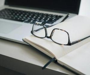 a laptop computer and an open book with a pair of glasses resting on top
