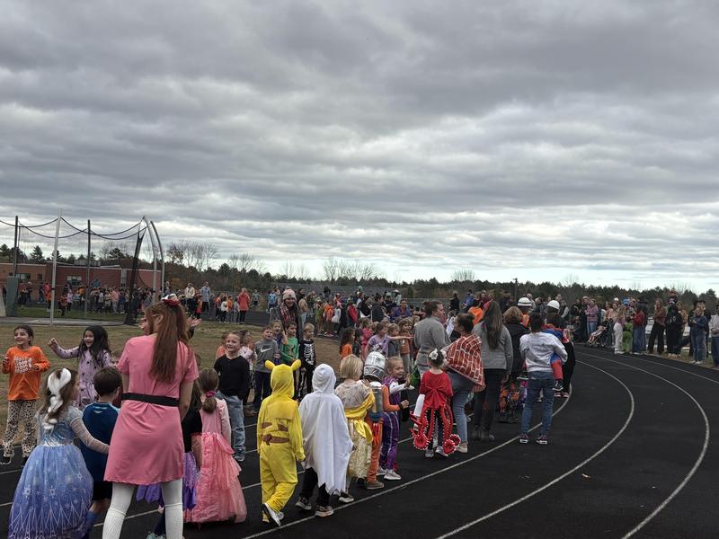 A large group of children in costumes lined up on a track under a cloudy sky.