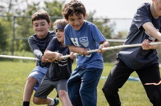 Four children happily playing tug-of-war on a grassy field.