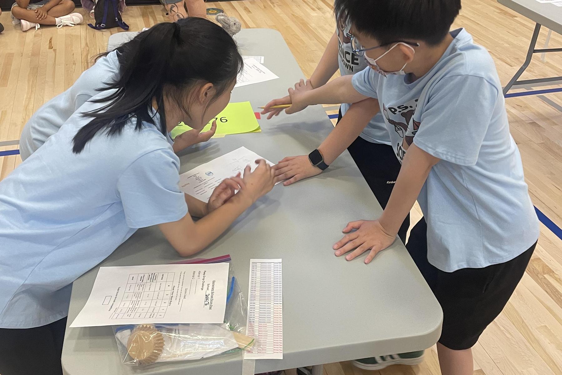 Children collaborate on a project at a table covered with papers and materials.