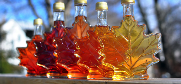 Five maple syrup bottles shaped like leaves, displaying various amber hues.