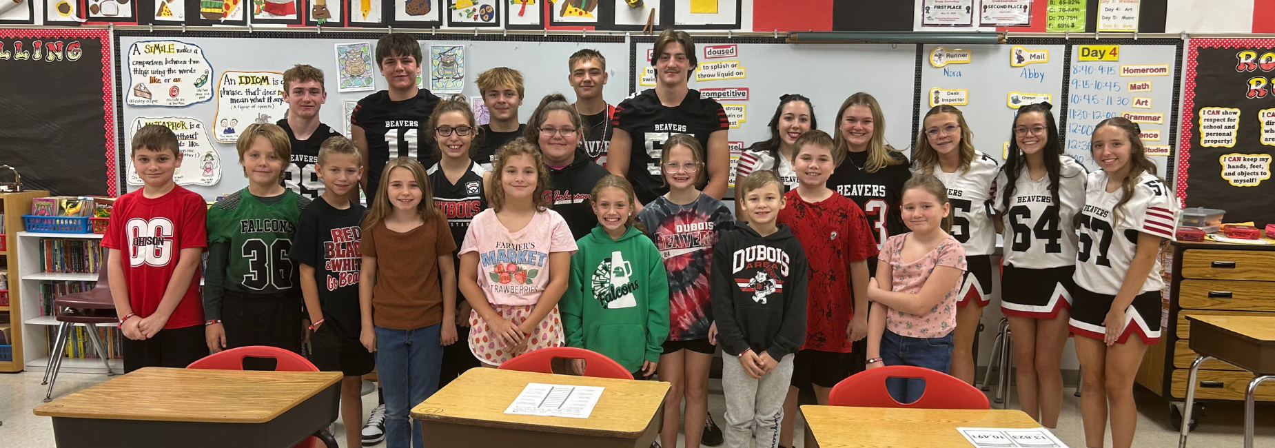 A large diverse group of students stands together in a classroom, all wearing matching clothing.