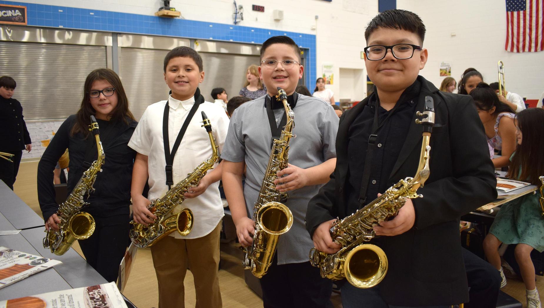 Four young musicians with saxophones pose together in a school setting.