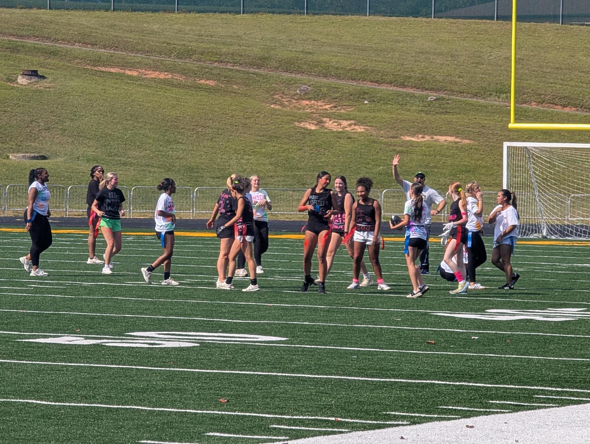 A group of girls playing flag football on a sports field during an outdoor event.