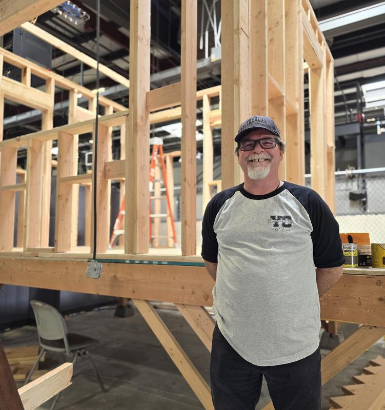 Image of a man standing in front of a framed out structure, smiling.
