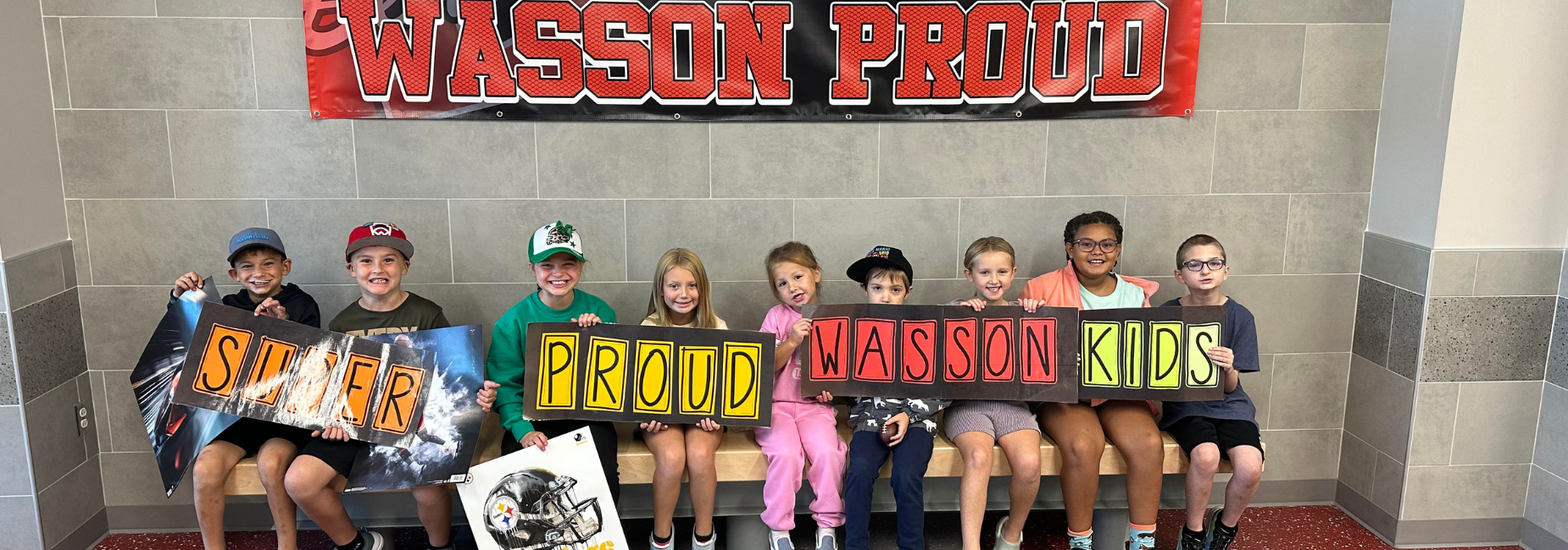 Eight kids displaying colorful signs that say 'Super Proud Wasson Kids' with a backdrop. Wasson Beaver Tail winners!
