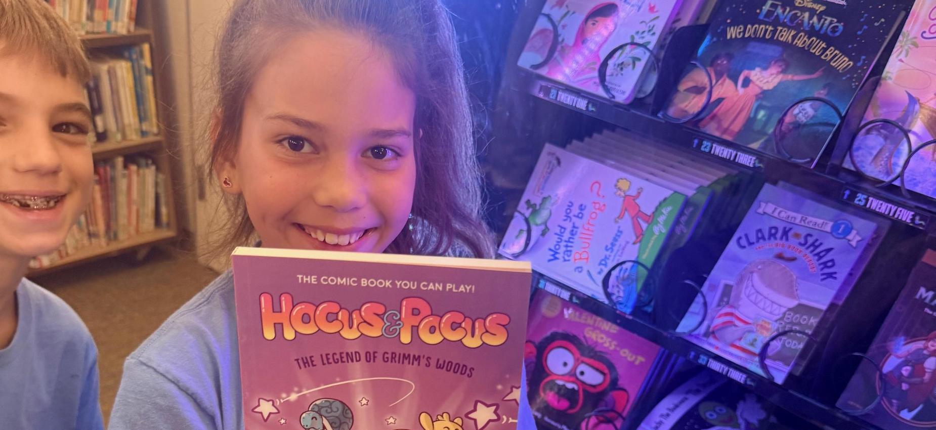 Child holding the book 'Hocus & Pocus' in a colorful book display.