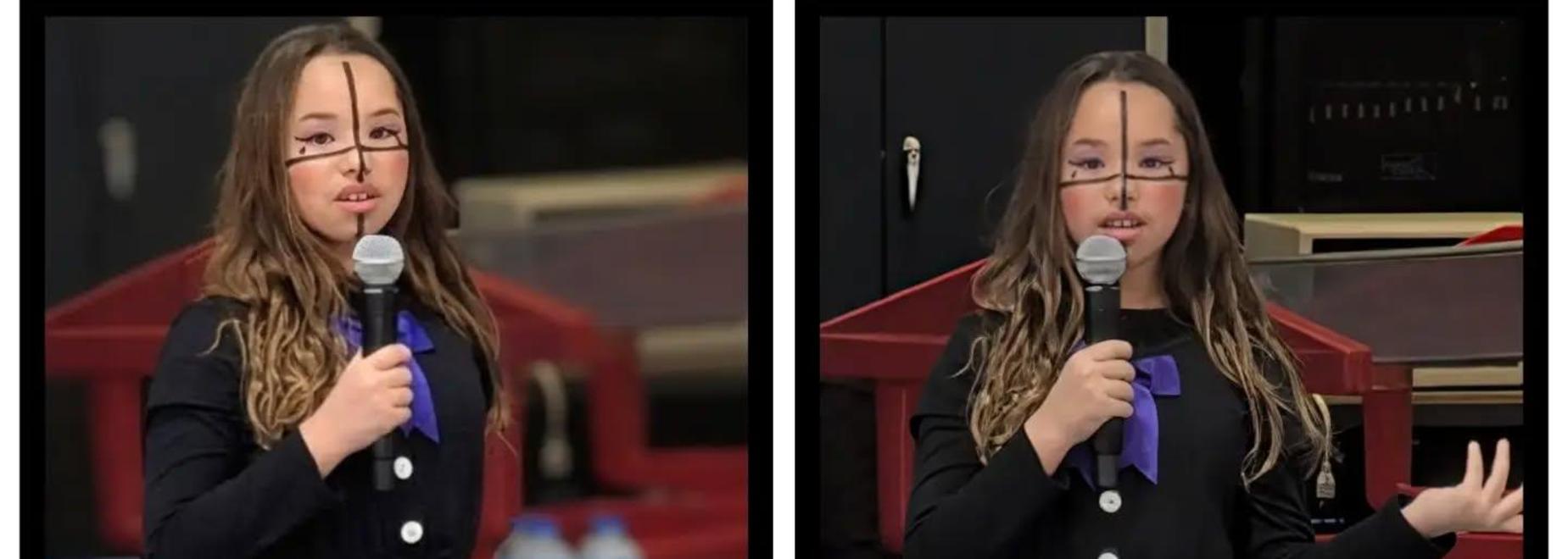 A girl in a black jumpsuit speaking at a school event.