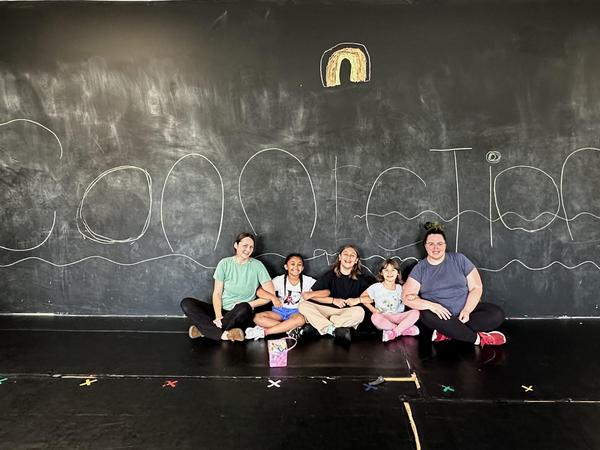 Five people sitting together on a black floor in front of a chalkboard with the word 'Connection' written on it.